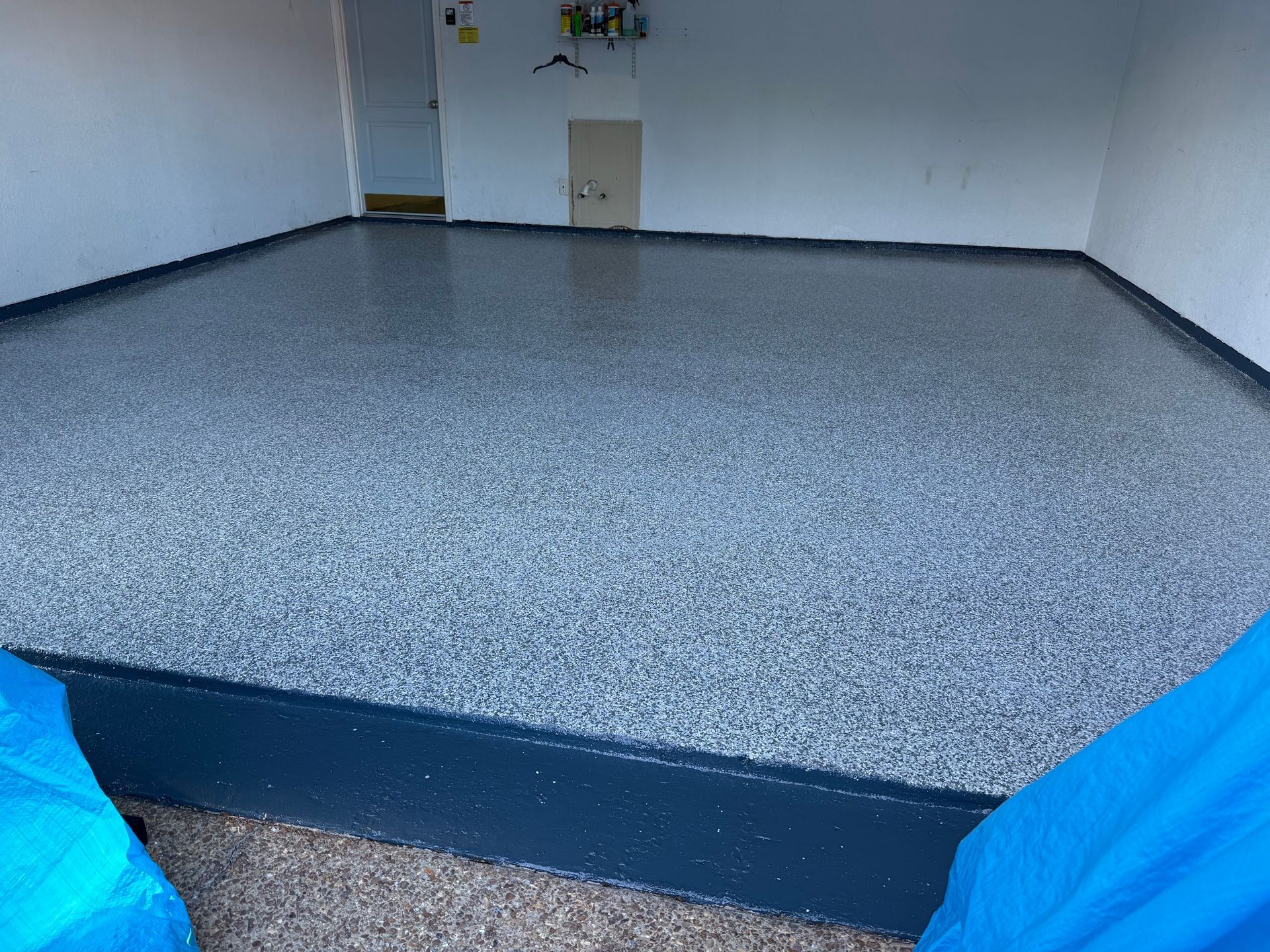 Garage with a newly finished epoxy floor in shades of gray. Walls are white.