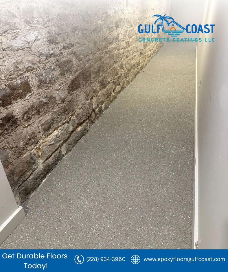 Epoxy floor installed along a stone wall. Gray speckled flooring. Gulf Coast logo in corner.