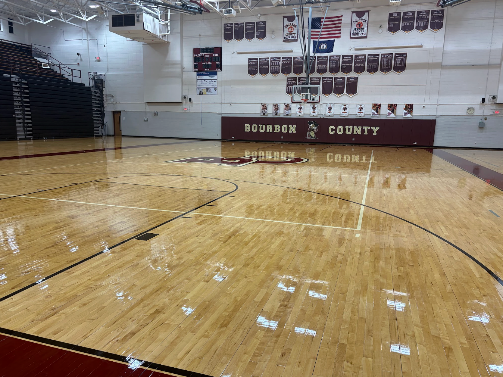 A polished hardwood basketball court inside a gymnasium with maroon and white wall banners reading