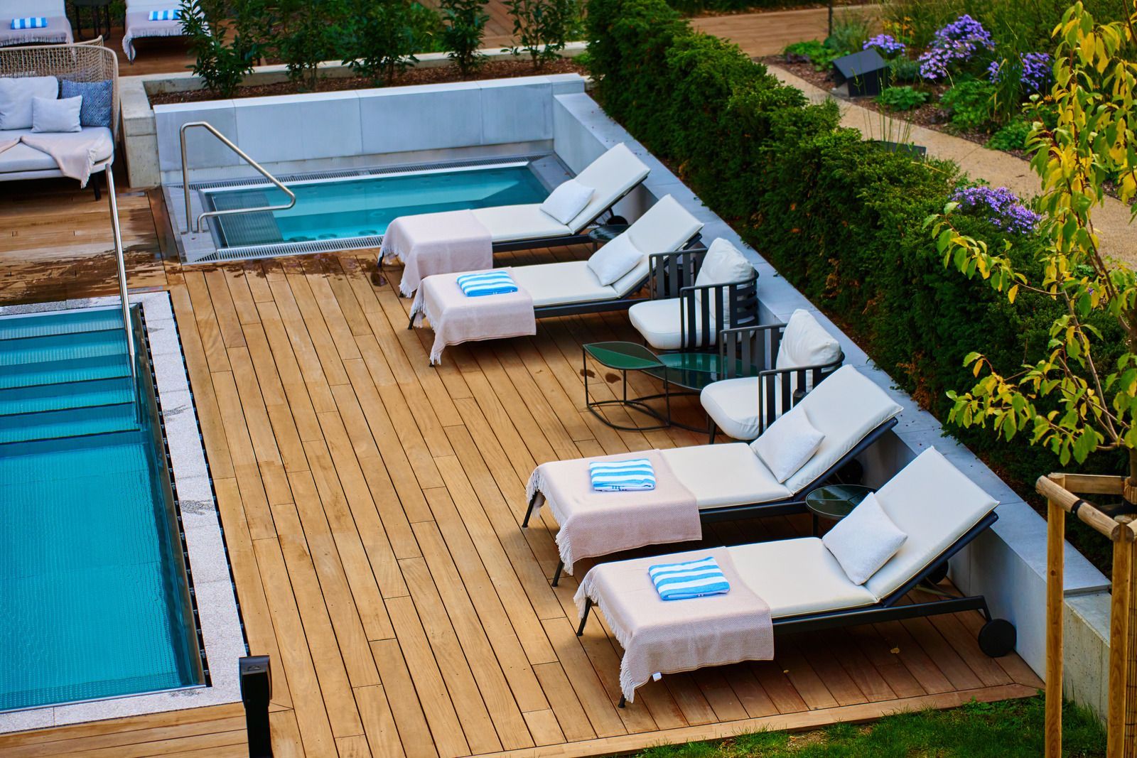 Swimming pool with rock waterfall, stone patio, green grass, and small palm trees.