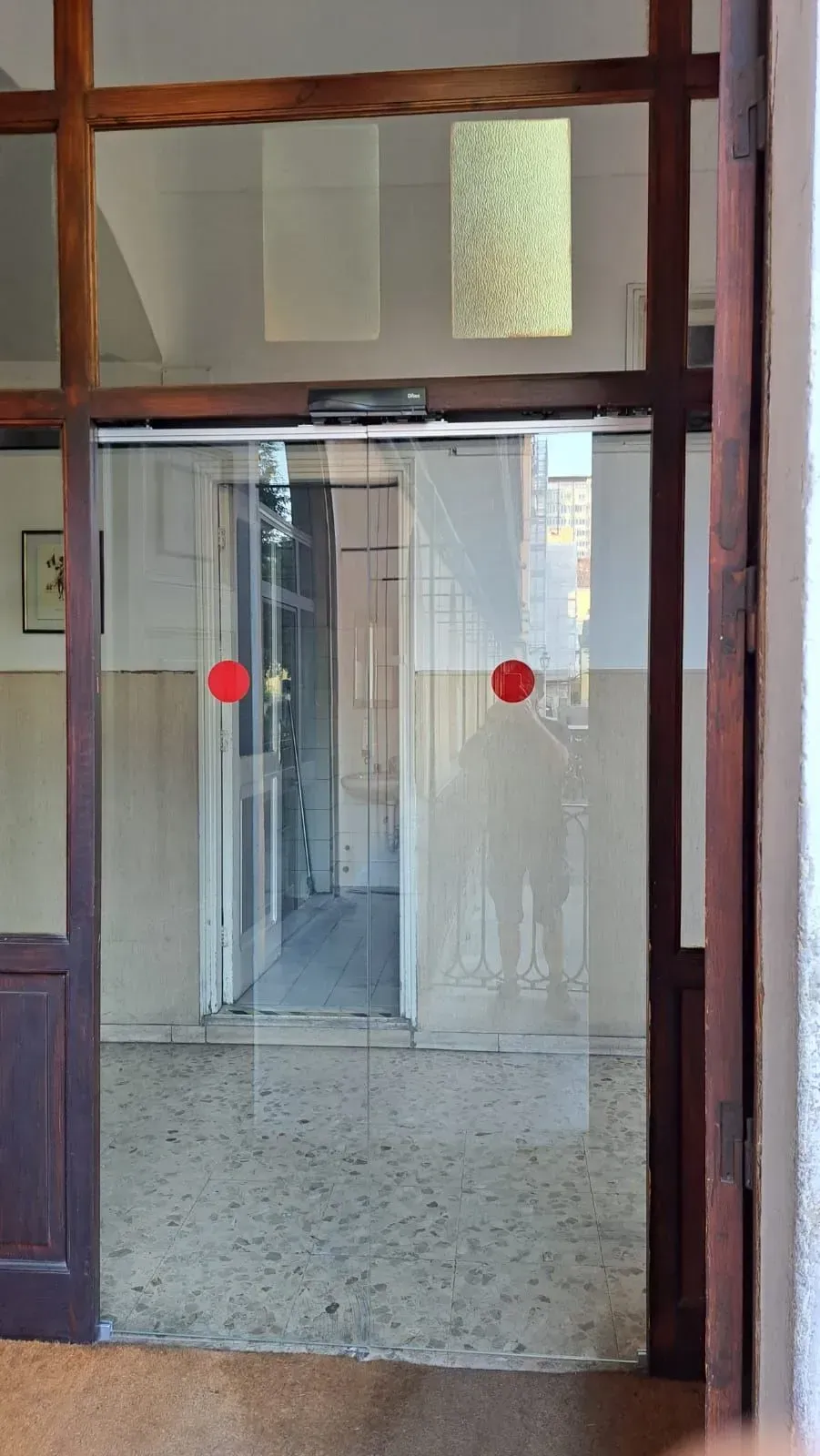 Corridoio interno con porta o divisorio in vetro, segnalato da due adesivi rossi.