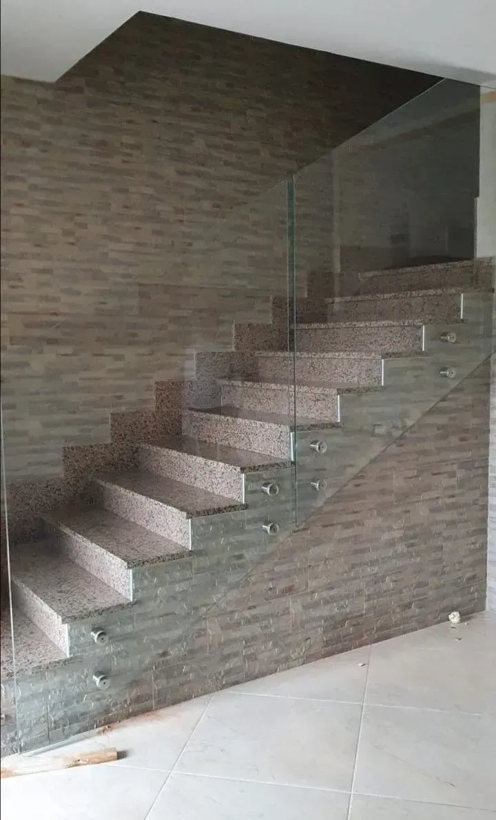 Scala interna moderna con gradini in pietra, parete in mattoni e ringhiera in vetro.