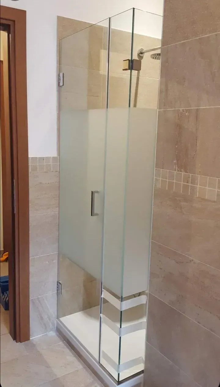Box doccia in vetro con pannelli satinati in un bagno piastrellato.