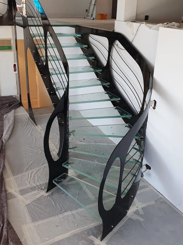 Scala con ringhiera nera e gradini in vetro in un cantiere, coperta da un telo protettivo in plastica.