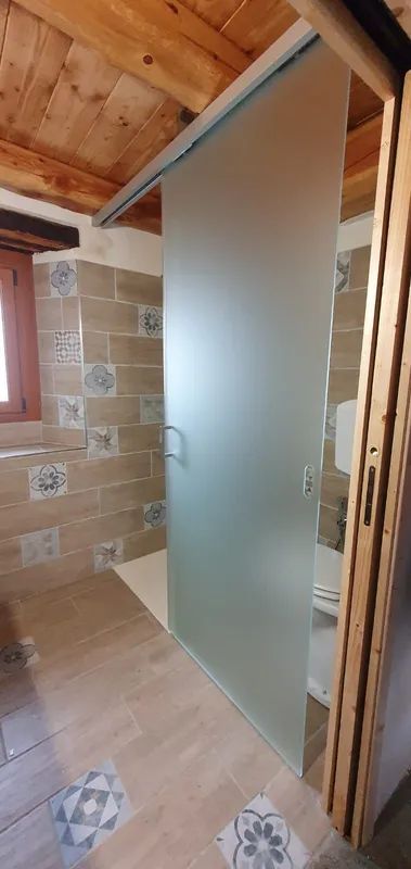 Piccolo bagno con parete rivestita in piastrelle di pietra, porta doccia in vetro satinato e soffitto con travi a vista.