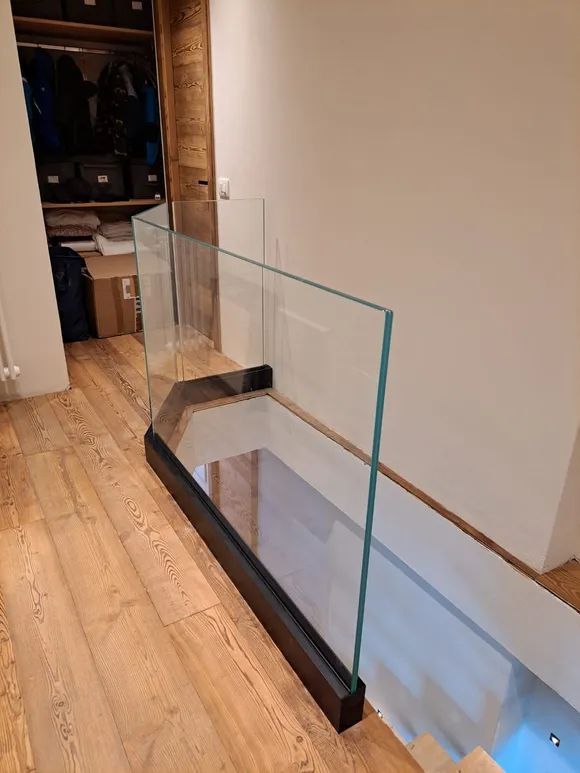 Ringhiera in vetro per scale installata lungo un corridoio accanto a un pavimento in legno e una parete bianca.