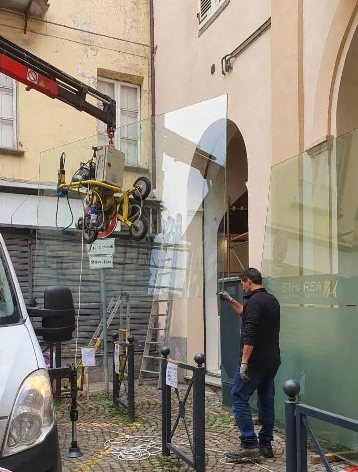 Un operaio e una gru sollevano attrezzature attraverso un vicolo accanto a un edificio con finestre ad arco.