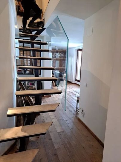 Corridoio interno con scala a vista, pavimento in legno e vista su una stanza luminosa oltre.