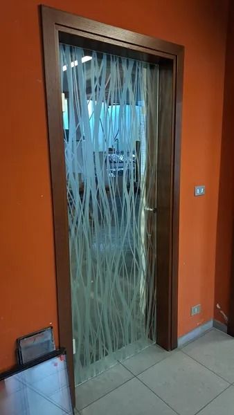 Porta a vetri con motivo ondulato satinato in un corridoio arancione, pavimento piastrellato a vista all'interno.