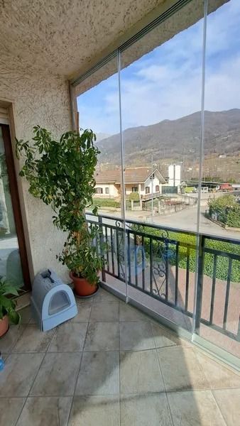 Balcone con piante in vaso, ringhiera blu e vista sulle montagne al di là di una piccola città