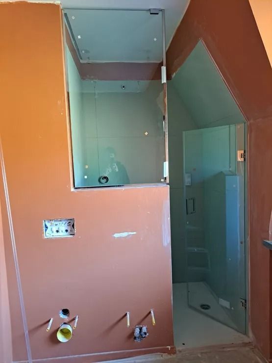Bagno non finito con pareti arancioni, zona doccia piastrellata e tubature a vista vicino a una porta.