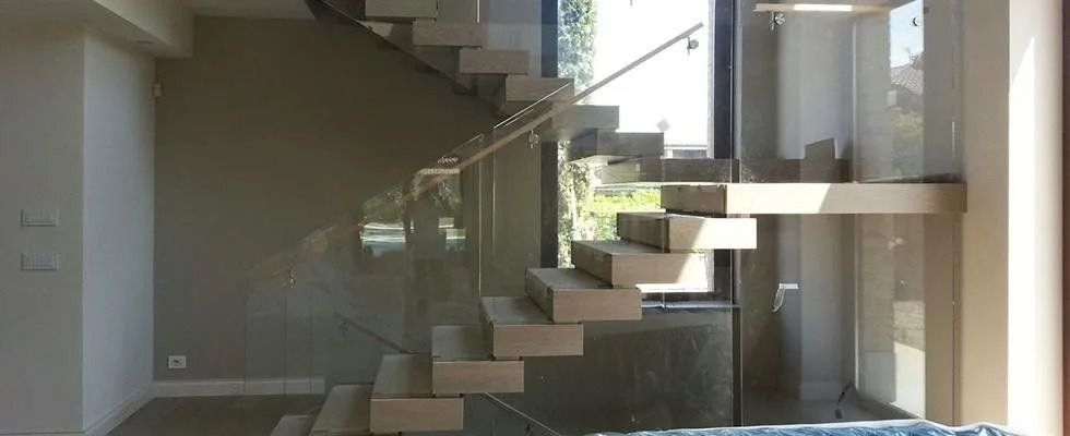 Scala interna moderna con ringhiera in vetro e luce solare che proietta ombre all'interno di una casa
