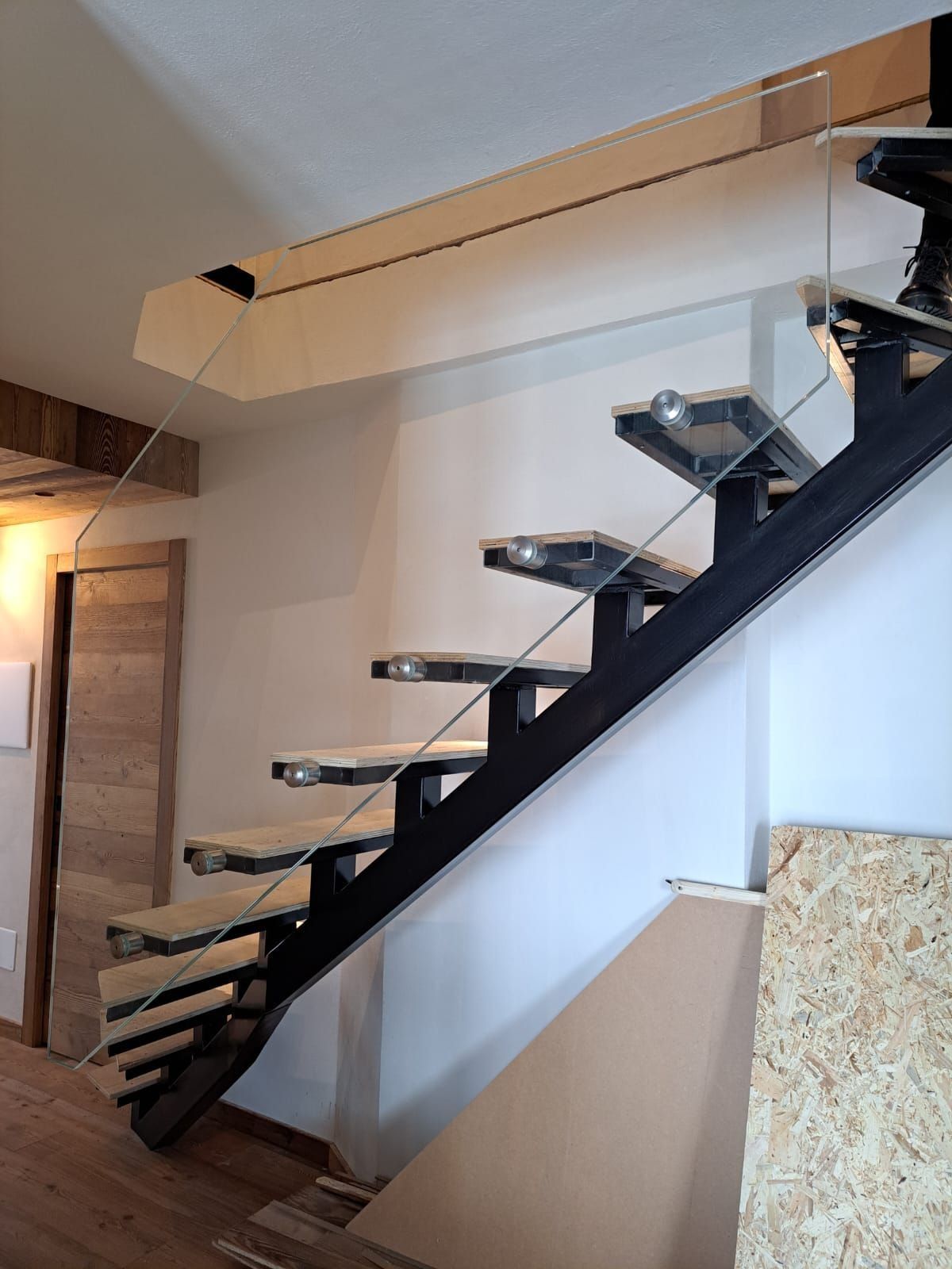 Scala moderna con gradini neri sospesi e ringhiera in vetro in un corridoio interno bianco.