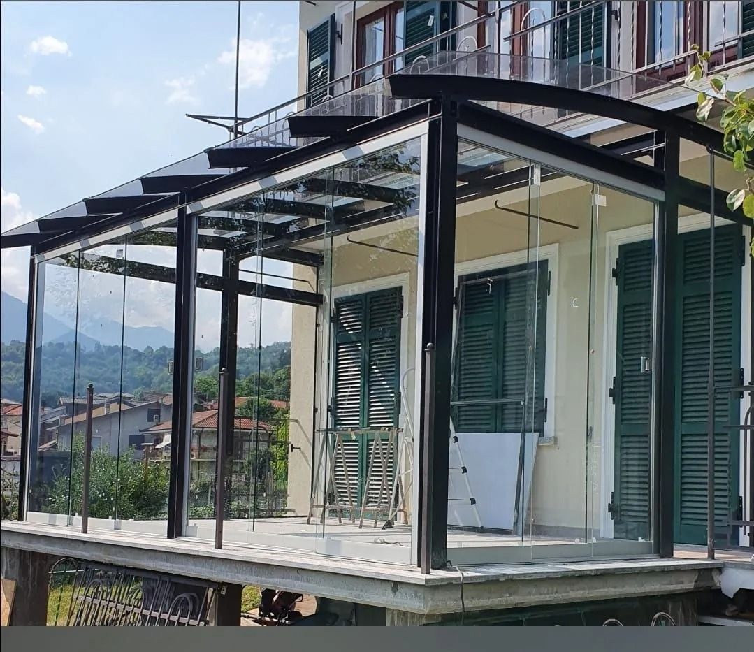 Moderno balcone vetrato con struttura in metallo nero su una casa in collina, con le montagne sullo sfondo.