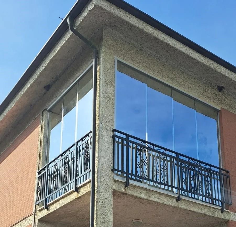 Balcone moderno di un appartamento con ringhiere nere e finestre blu riflettenti su un edificio beige e in mattoni.