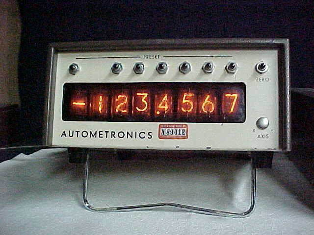 Vintage Autometrics electronic counter with glowing orange digits and a gray metal faceplate on a stand