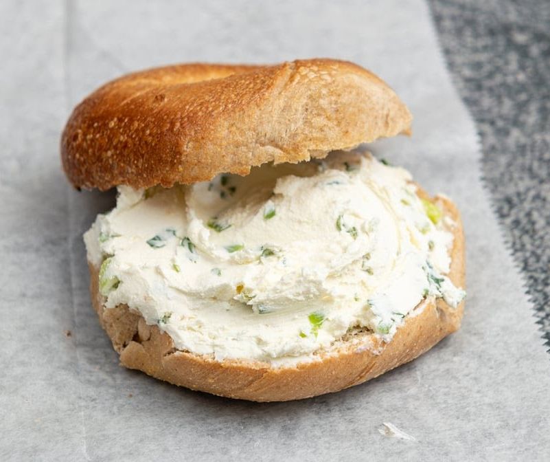 A bagel with cream cheese on it is sitting on a piece of wax paper.