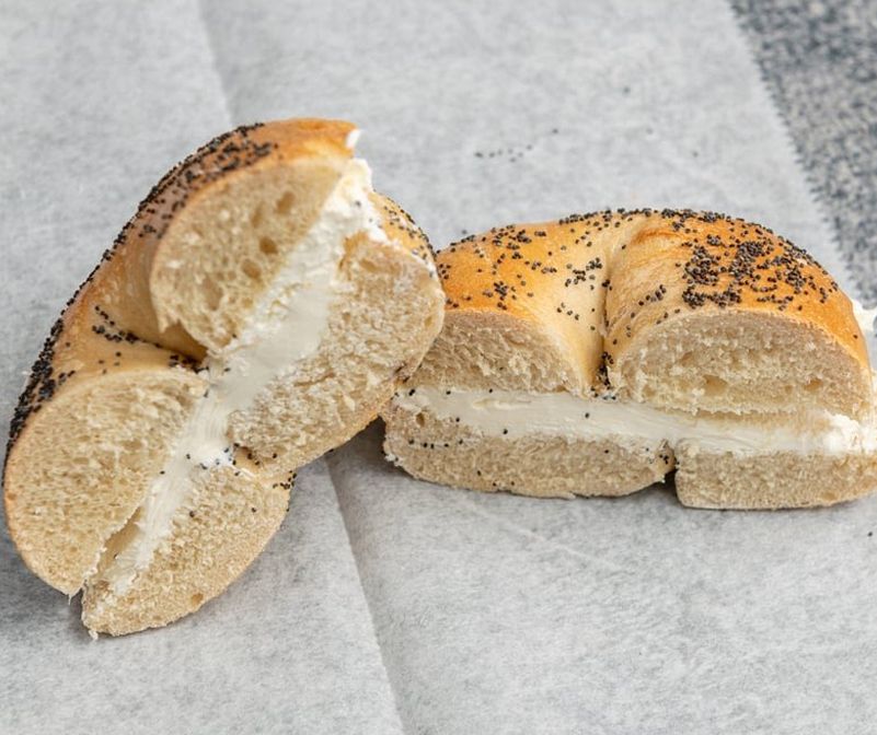 A bagel with cream cheese and poppy seeds is cut in half.
