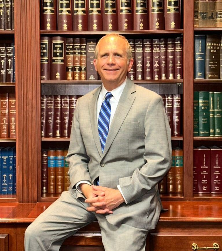 A man in a suit and tie is sitting in front of a bookshelf