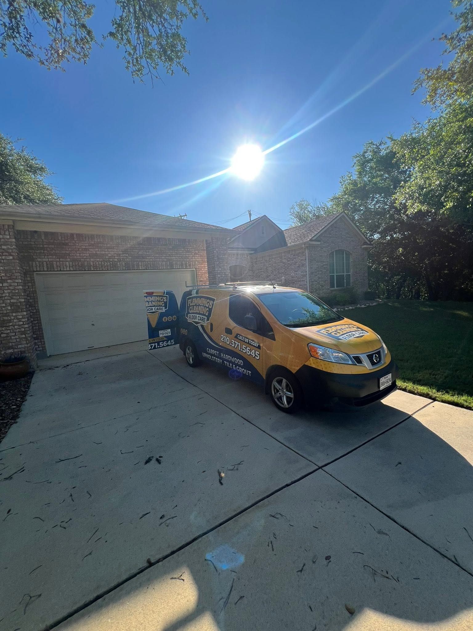 Yellow van parked in a sunny driveway beside a brick house and garage.