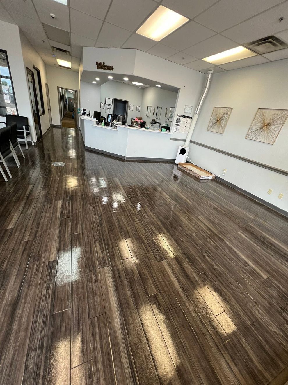 Empty office lobby with glossy wood floor, white walls, and a front reception desk.