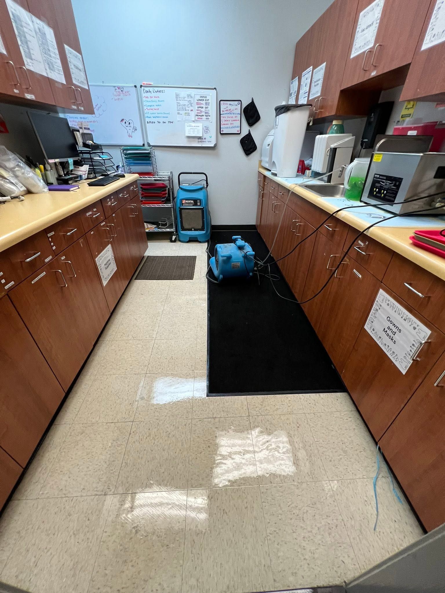 Narrow lab workspace with countertops, cabinets, posters, and a blue vacuum on the floor in the center aisle