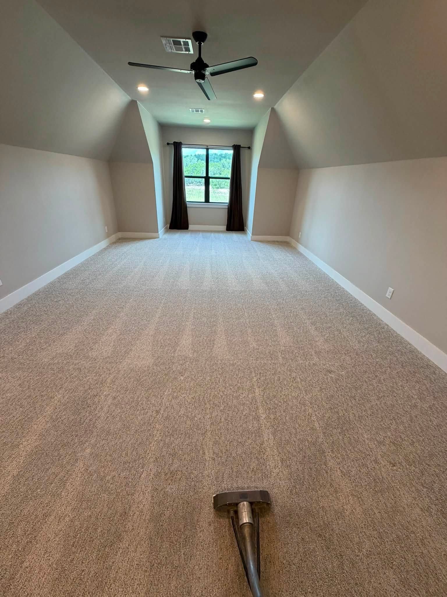 Long carpeted attic room with sloped ceilings, recessed lights, and glass doors at the far end.