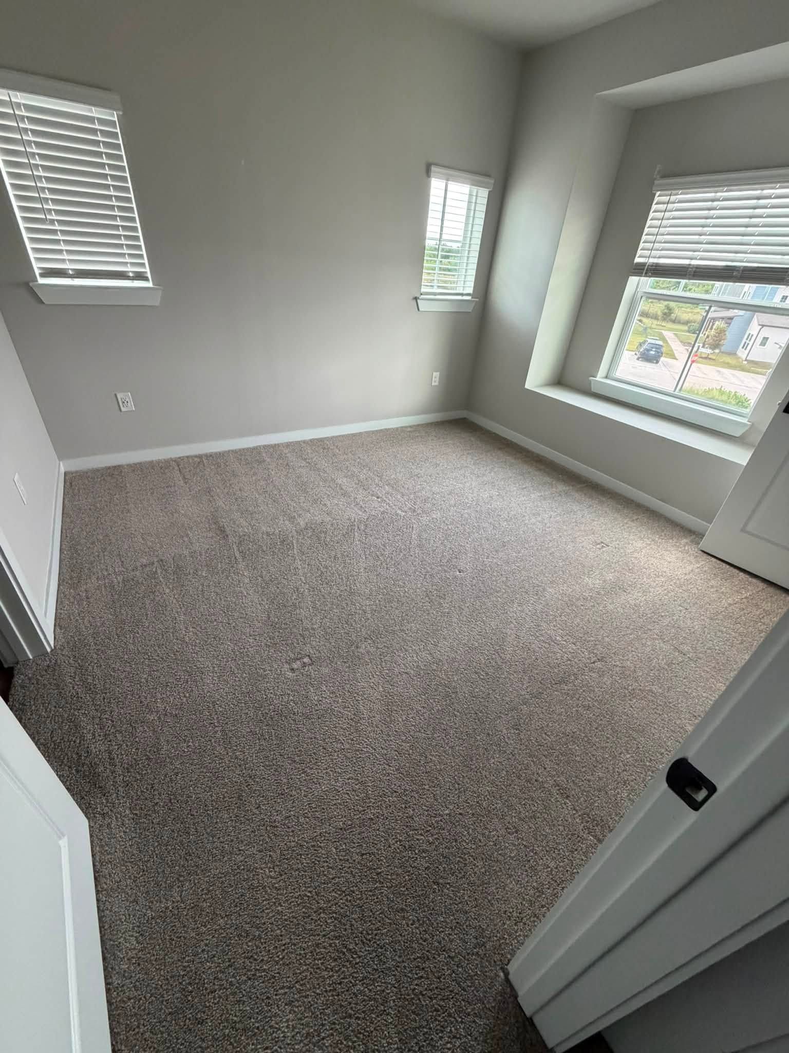 Empty carpeted bedroom with three windows and white walls, viewed from the doorway