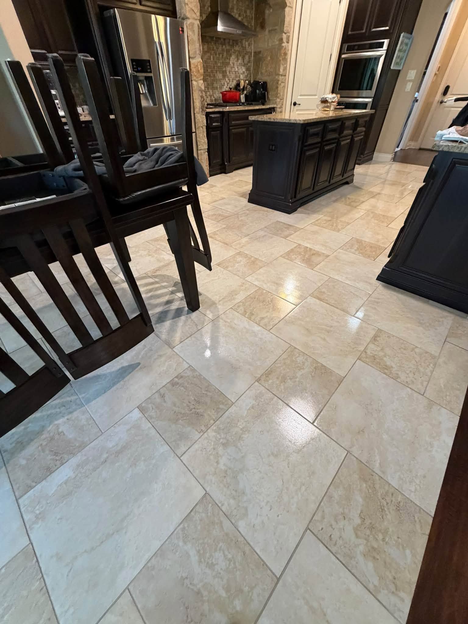 Modern kitchen with beige tile floor, dark cabinets, and dining chairs in the foreground