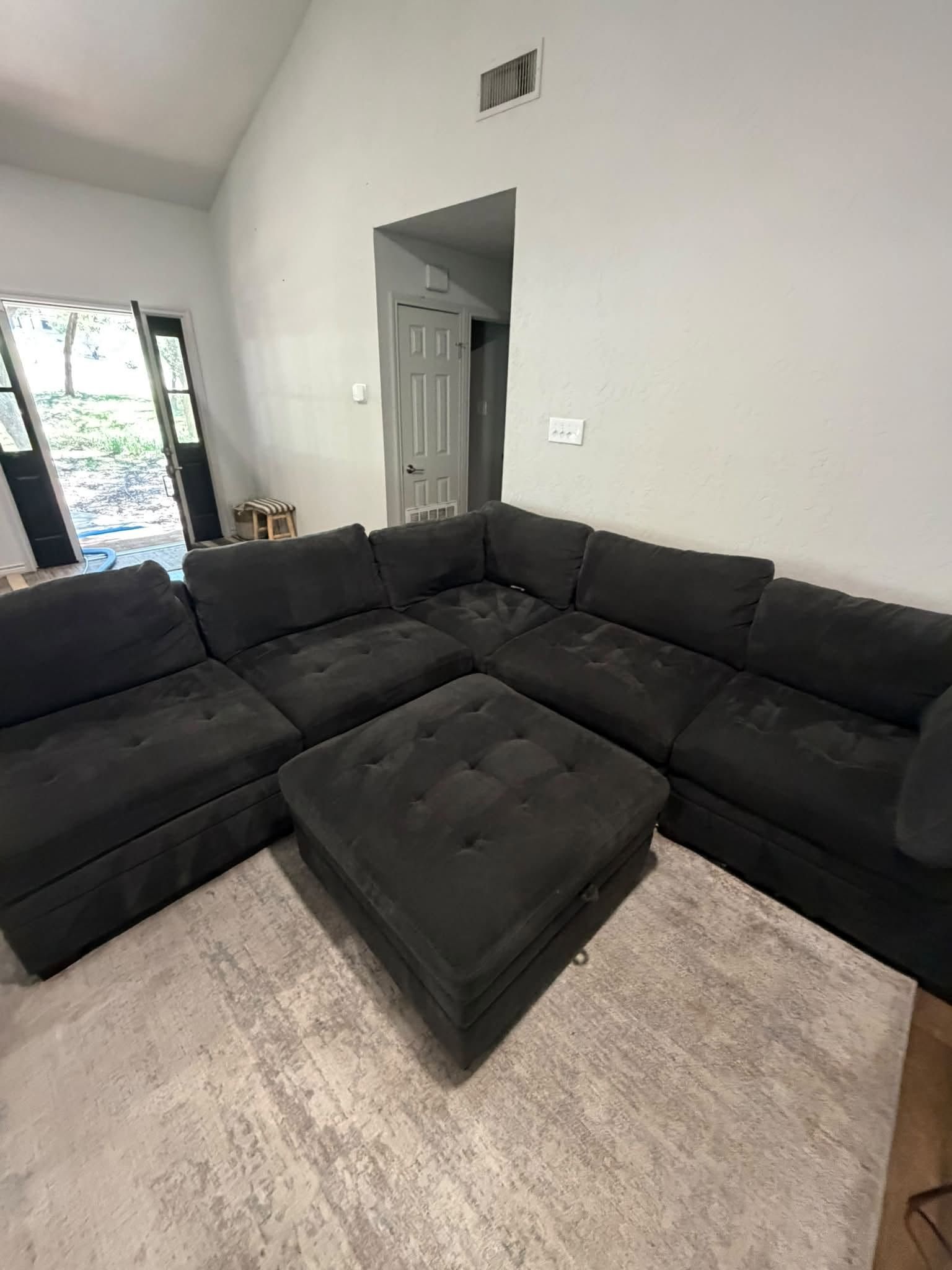 Black sectional sofa with ottoman in a bright living room with gray walls and tiled floor