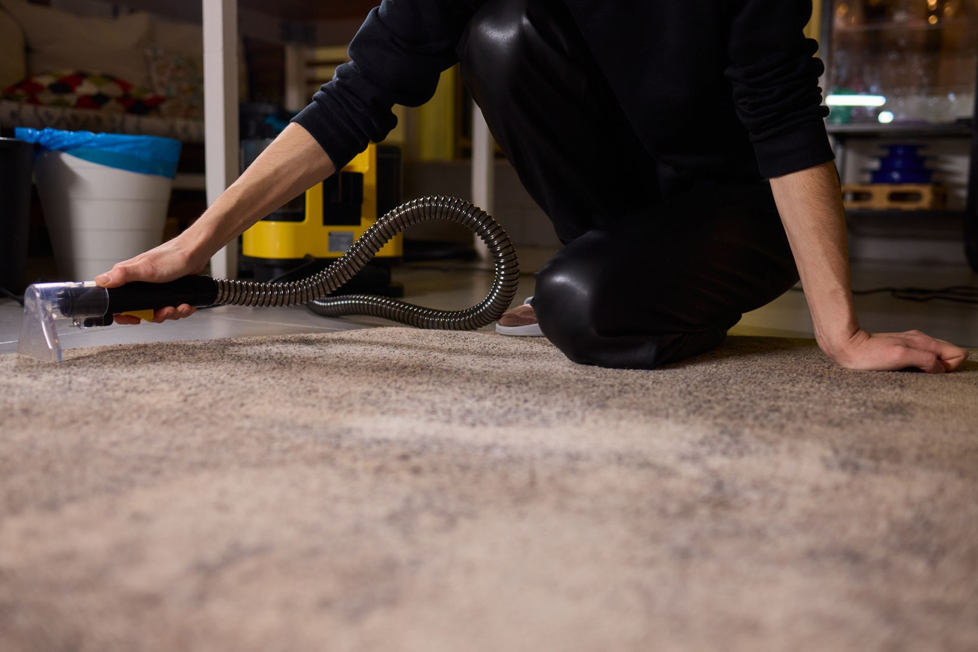 Person vacuuming a carpeted floor with a hose attachment in a home interior