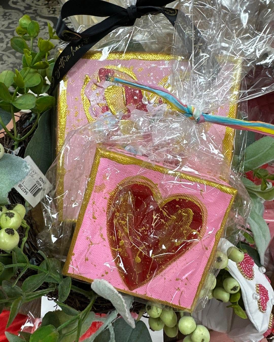 Pink glittery heart ornaments with gold trim, wrapped in clear plastic and decorated with green foliage and berries
