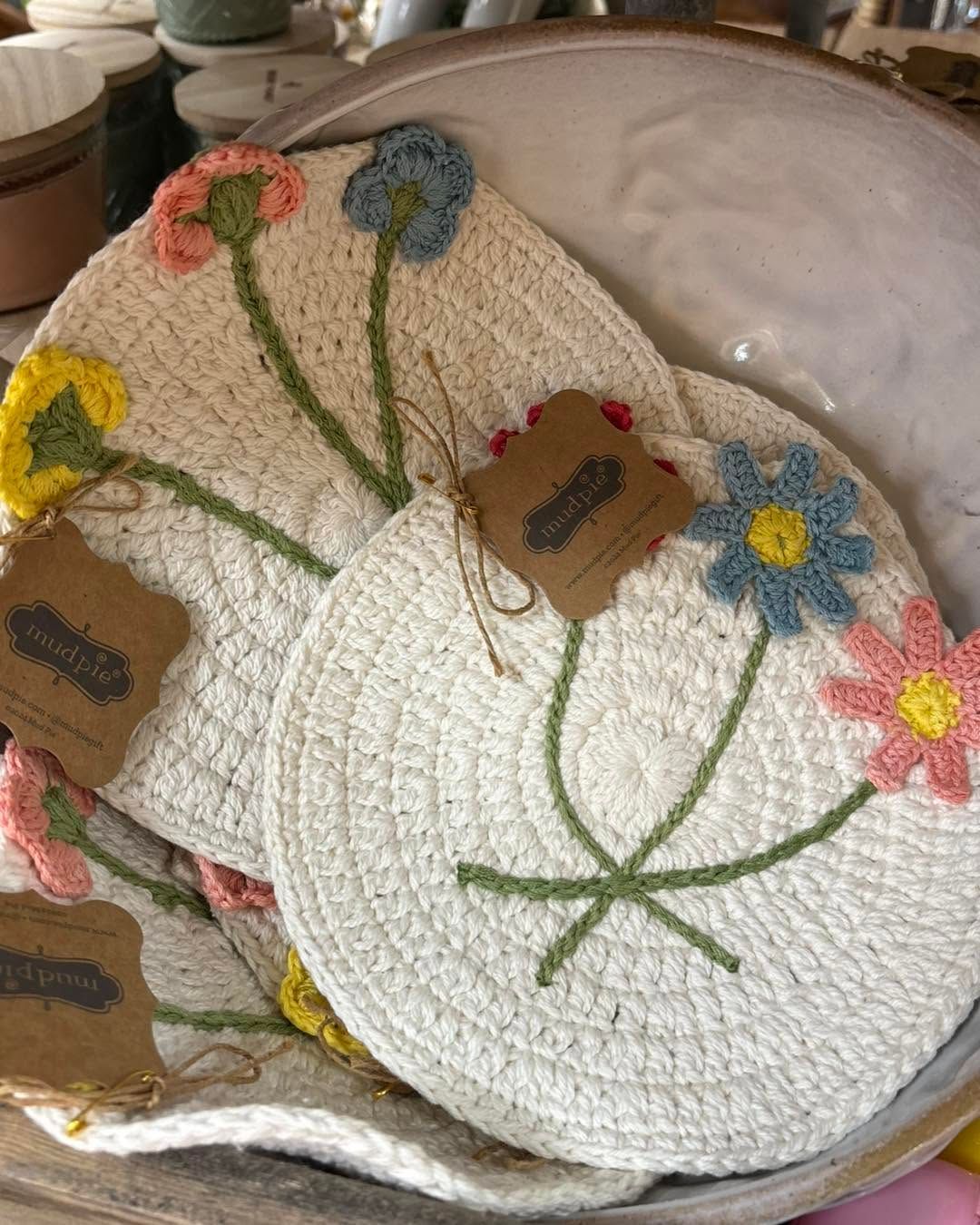 Crocheted white pot holders with colorful floral embroidery stacked in a bowl