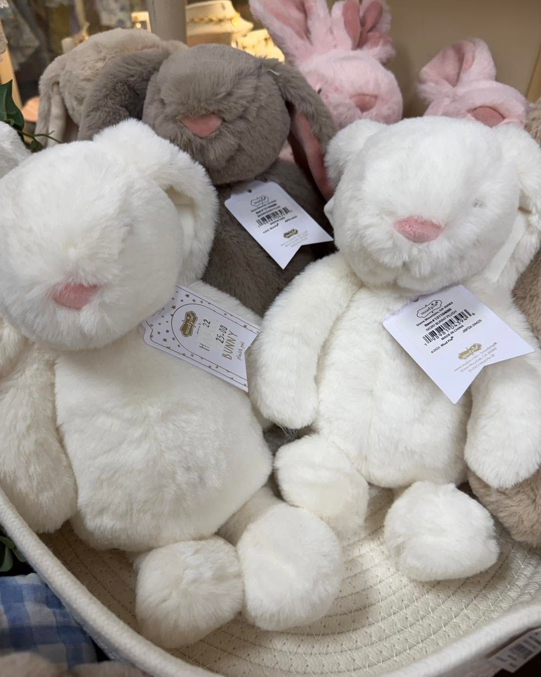 Plush white and gray stuffed bunnies with pink ears and tags in a basket