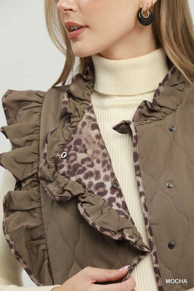 Woman in a ruffled brown jacket over a cream turtleneck, shown in a close-up fashion portrait.