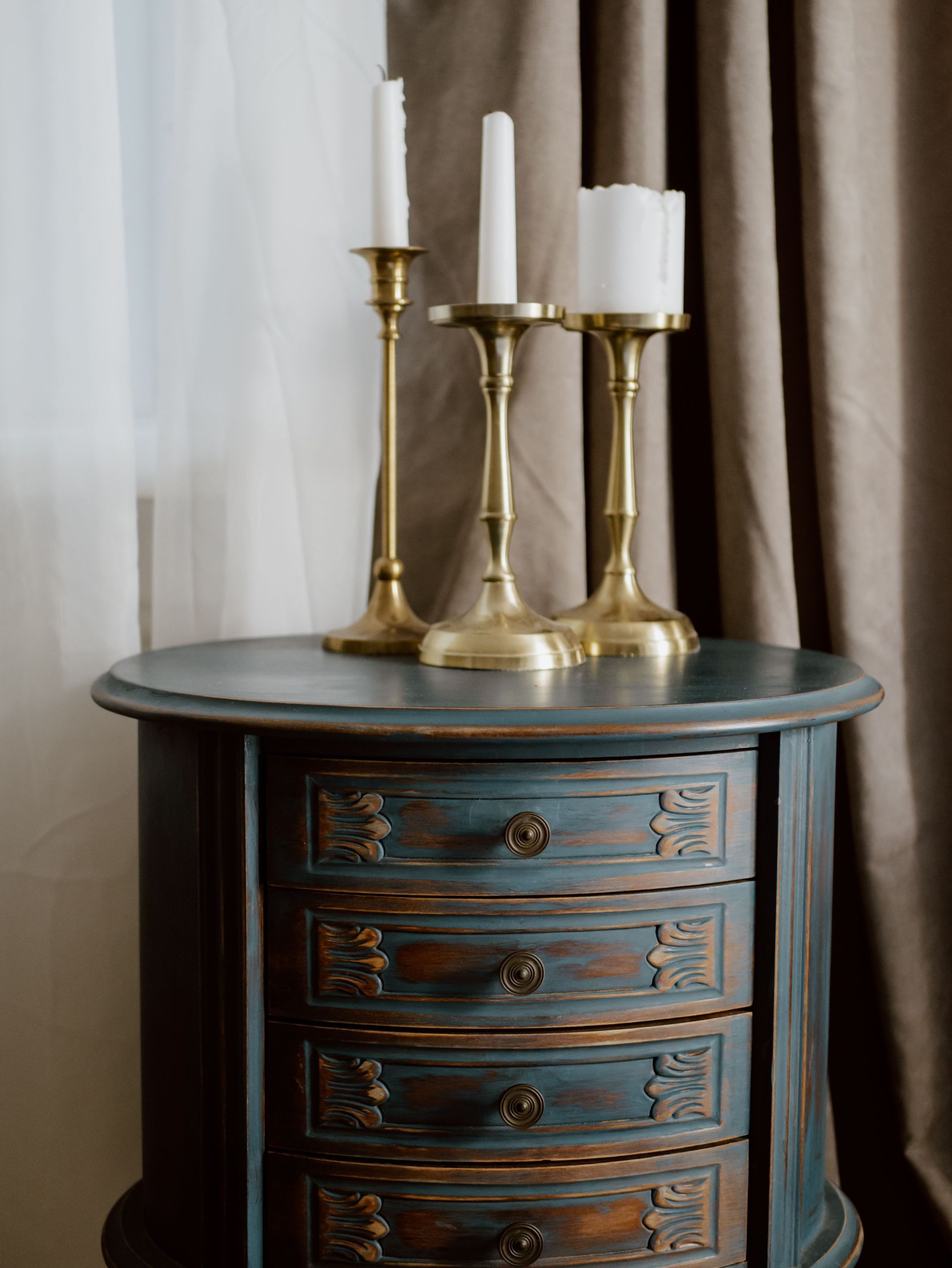 Vintage blue dresser with brass candlesticks and white candles beside curtains