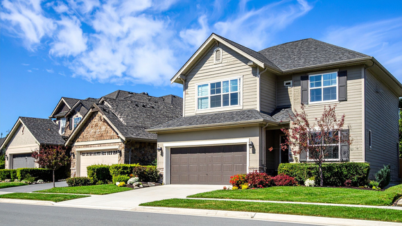 Suburban house with stone facade, gray roof, attached garage, and green lawn on a sunny day