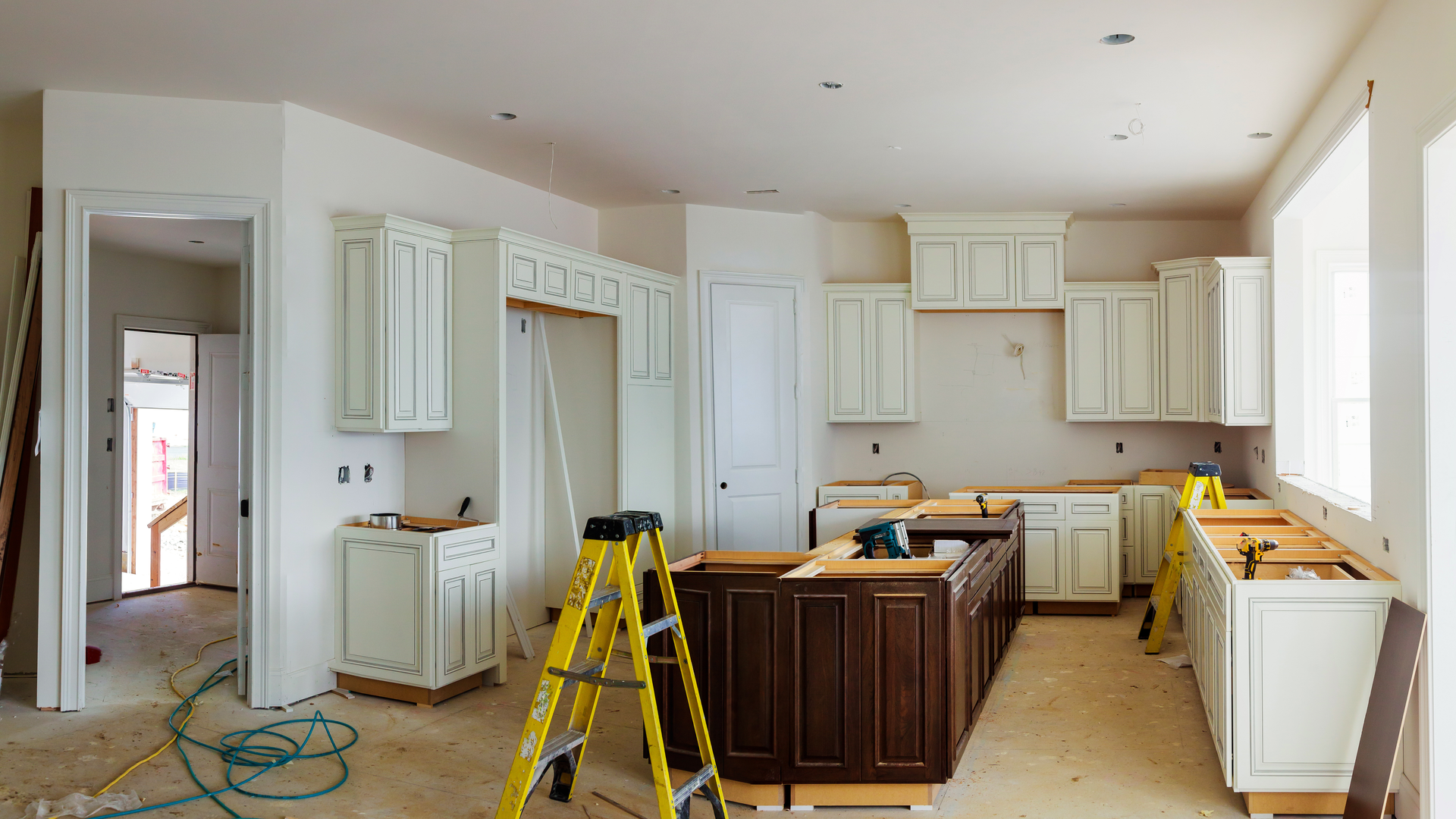 Kitchen under renovation with white cabinets, island, and a yellow step ladder in the center