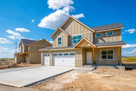 New two-story suburban house with beige siding, white garage doors, and a concrete driveway under a blue sky