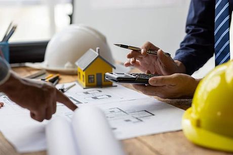 Architect reviewing blueprints with a yellow house model and hard hat on a desk