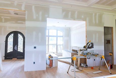 Renovated living room with drywall, tools, and a miter saw on a workbench near large windows