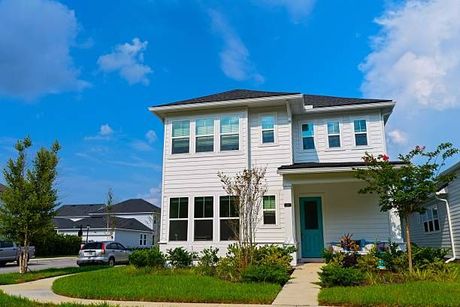Two-story white house with a teal door and green lawn under a bright blue sky