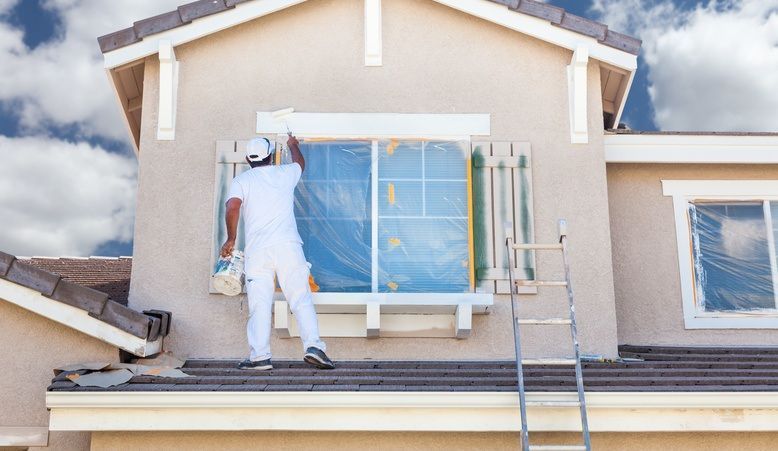 A man is painting a window on the side of a house.