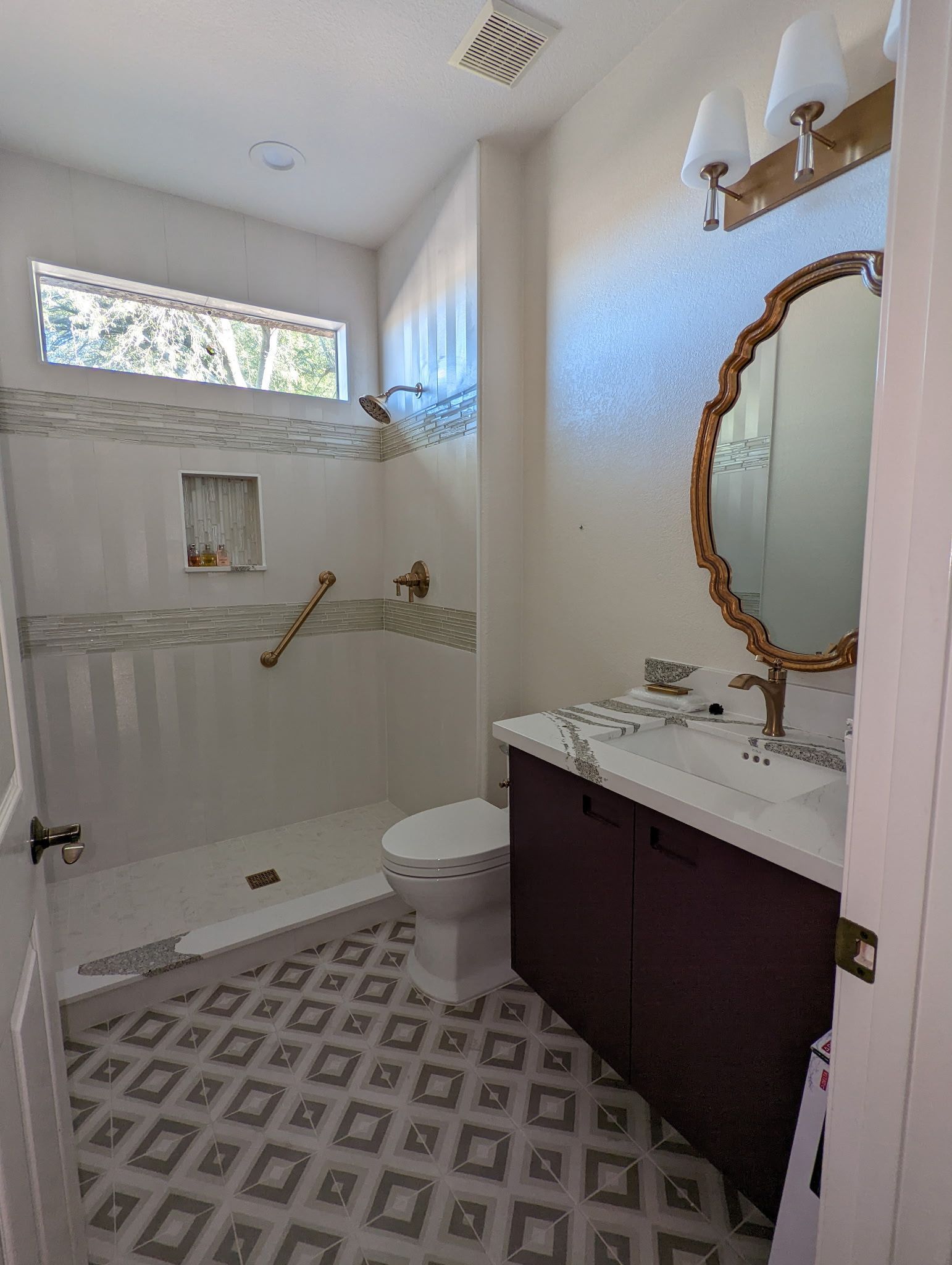 Bathroom with white walls, patterned floor tiles, dark vanity, ornate mirror, and shower.