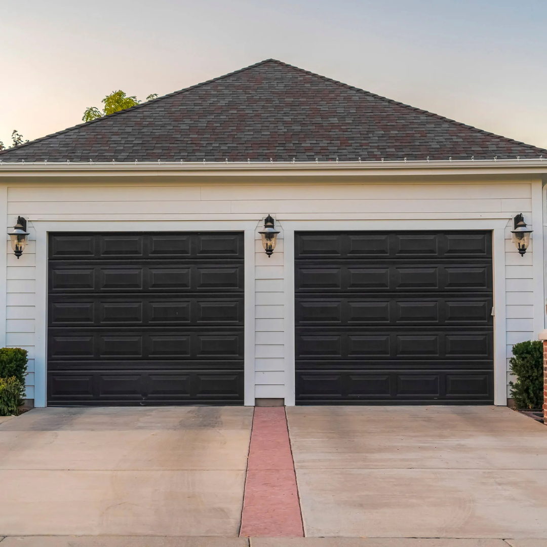 A white house with two black garage doors and a brick roof.