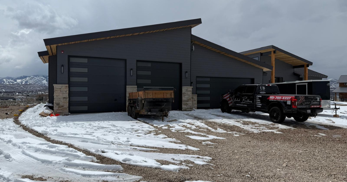 Gray modern house with two garage doors, a pickup truck, and patchy snow on the ground