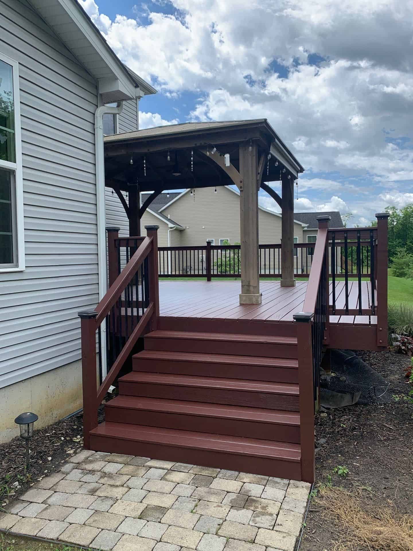 Raised wooden deck with stairs and pergola beside a house, with a brick patio below