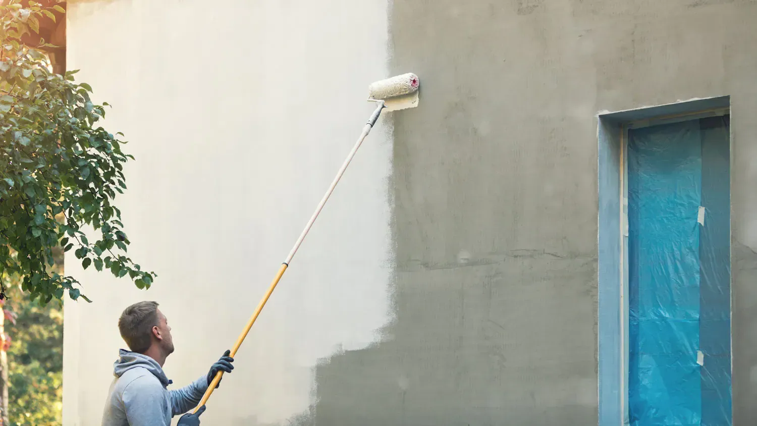 A man is painting a wall with a paint roller.