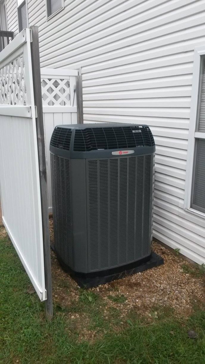 An air conditioner is sitting on the side of a house next to a white fence.