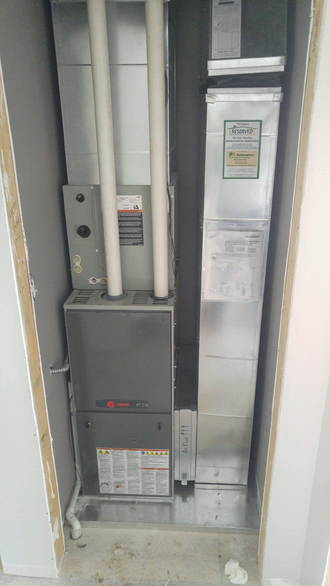 A furnace is sitting in a corner of a room next to a wall.